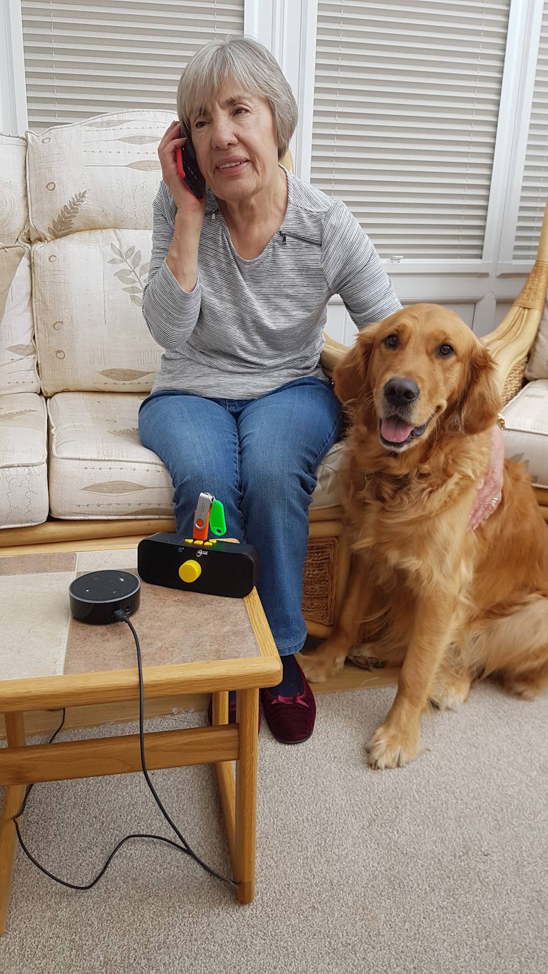 Woman listening to Ellesmere Port and Neston Talking newspaper while sitting on a couch with her guide dog sitting next to her